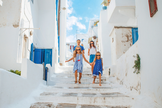 Familie mit zwei Kindern in wei&szlig; blauen Klamotten l&auml;uft eine wei&szlig;e Gasse in einem griechischem Ort hinunter