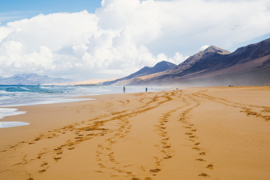 Breiter Strand auf Fuerteventura, links das Meer, im Hintergrund Felsen und etwas Nebel